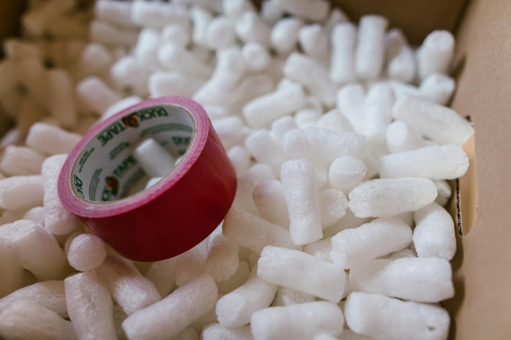 Close-up of red duct tape on packing peanuts in a cardboard box for shipping or moving.
