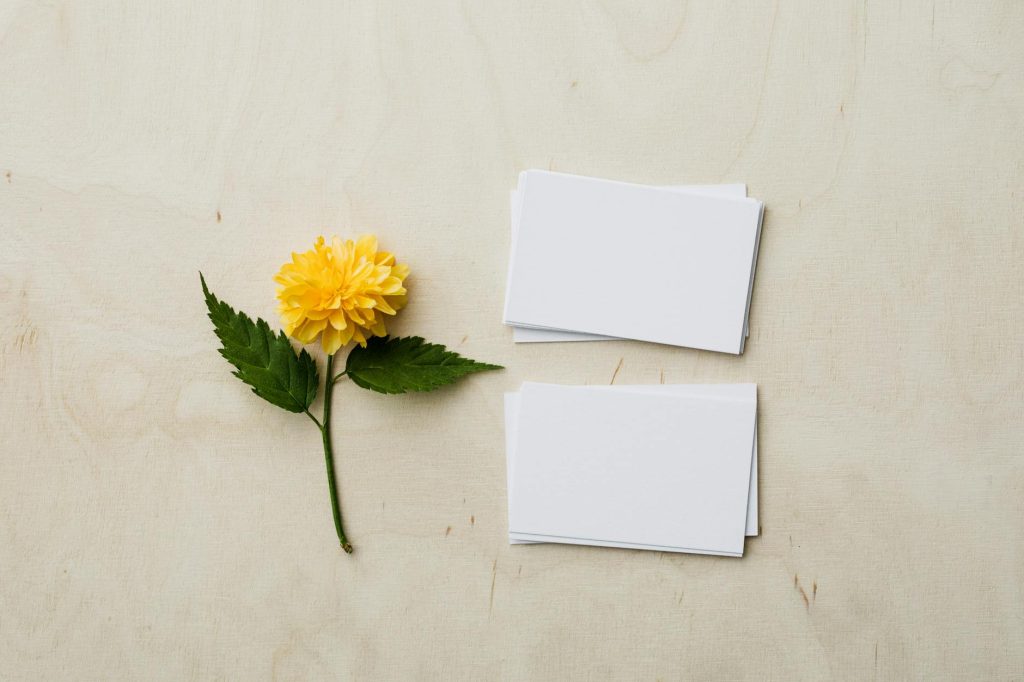 Flat lay of blank business cards next to a yellow flower on a wooden surface.