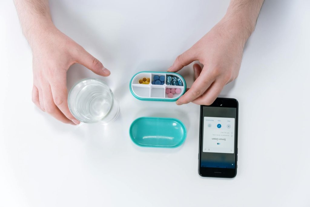 Overhead view of hands using a smartphone app and pill organizer for medication management.