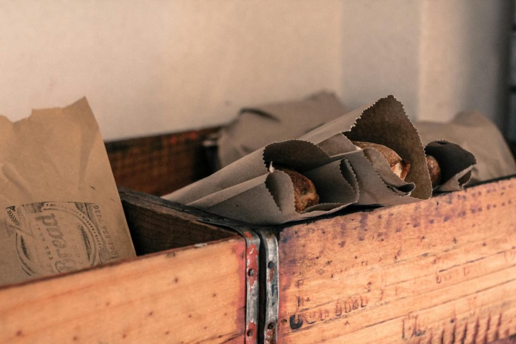 Artistic photo of freshly baked bread wrapped in brown paper, placed inside a rustic wooden crate.