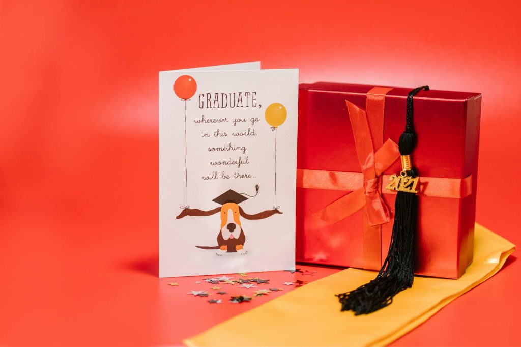 Celebrate graduation with a festive card, gift box, and tassel on a vibrant red backdrop.