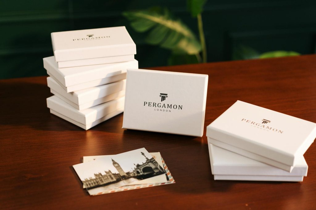 Stylish white Pergamon London gift boxes displayed elegantly on a wooden desk with photos.