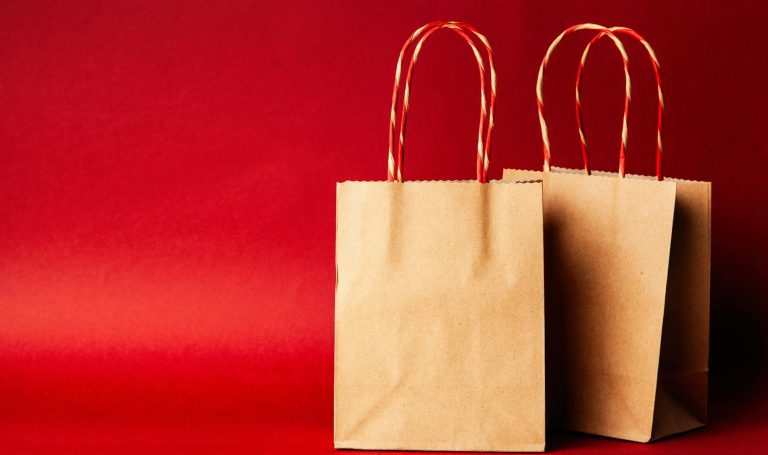 Simple brown paper bags with handle on a festive red backdrop, perfect for Christmas.