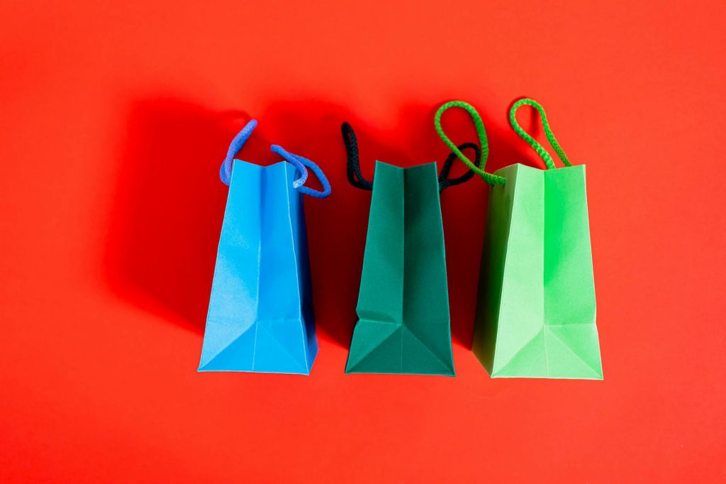 Three colorful paper shopping bags on a striking red backdrop, ideal for shopping and sale themes.