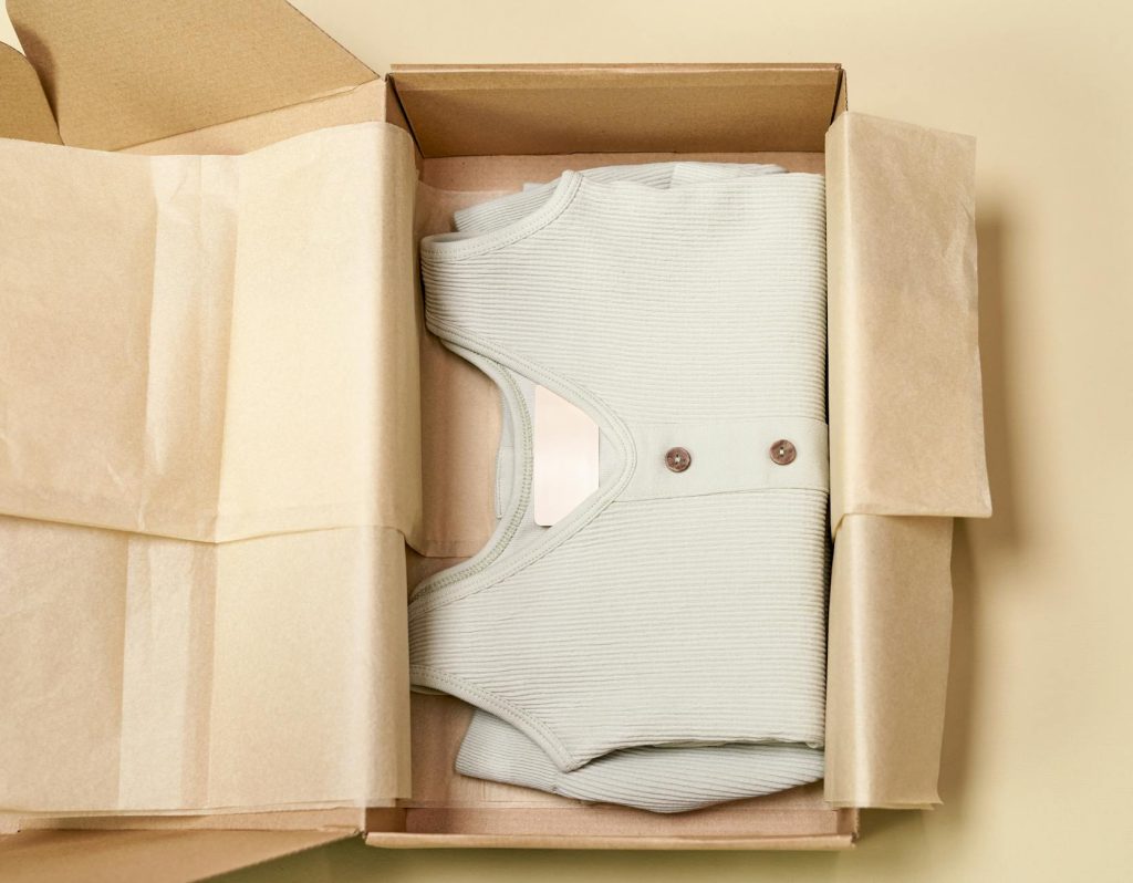 Minimalist packaging showcases a ribbed beige garment neatly folded inside a cardboard box.