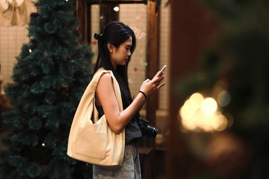 Young woman engages with her smartphone, surrounded by festive indoor Christmas decorations.