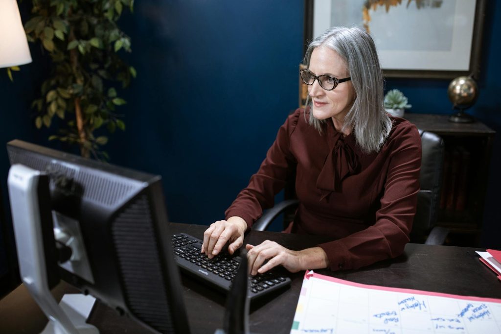 Elderly woman working on a computer in a modern office setting, focused and engaged.