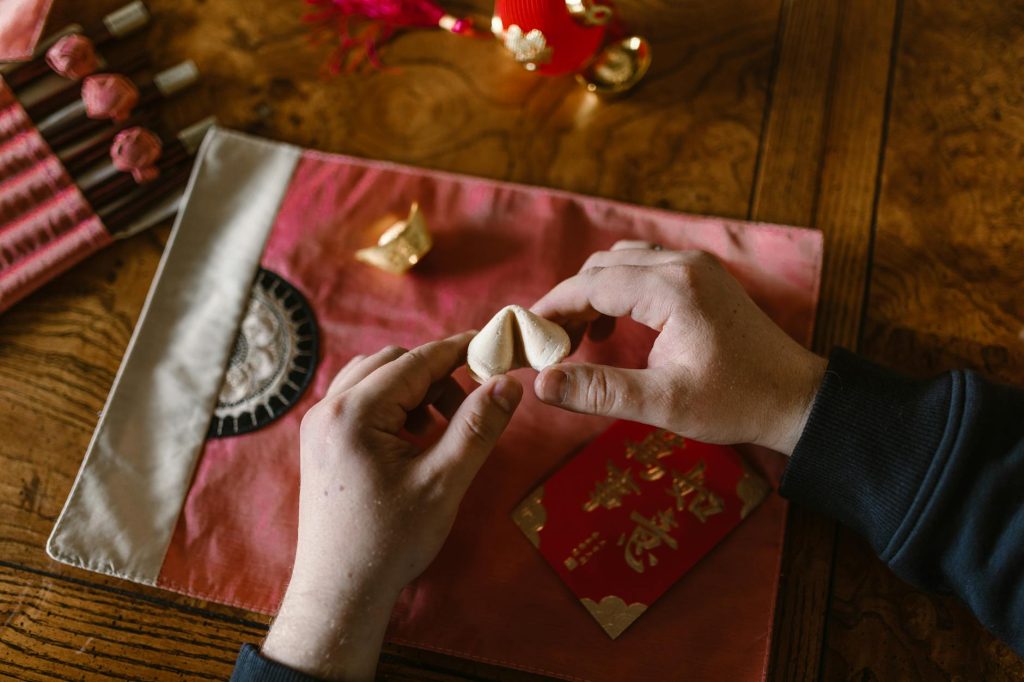 Hands holding a fortune cookie above a red envelope, symbolizing luck and tradition.