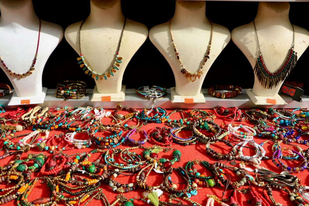 Colorful handmade jewelry showcased on mannequins at an outdoor market.