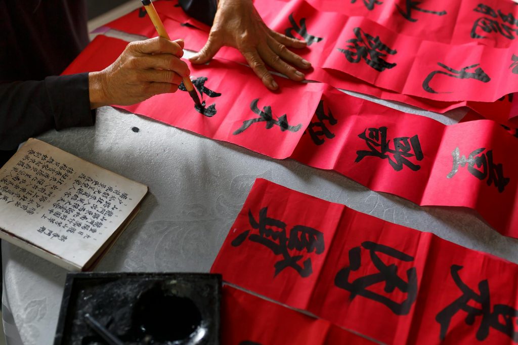 Artist creating traditional Chinese calligraphy on red paper for cultural celebration.