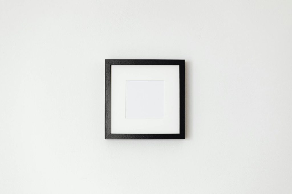 Simple black picture frame hanging on a white wall for mockup purposes.