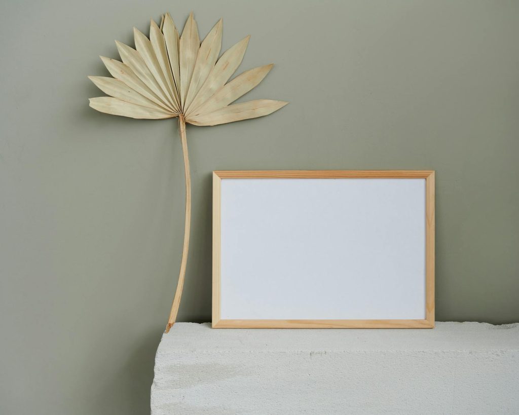 A wooden frame and dried palm leaf on a textured surface against a muted green wall.