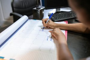 Close-up of a woman planning her schedule on a desk calendar in an office setting.
