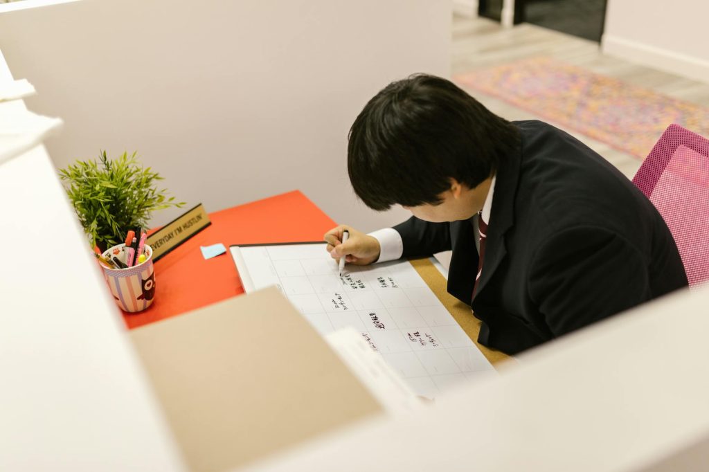 Business professional writing on monthly calendar at desk in modern office.