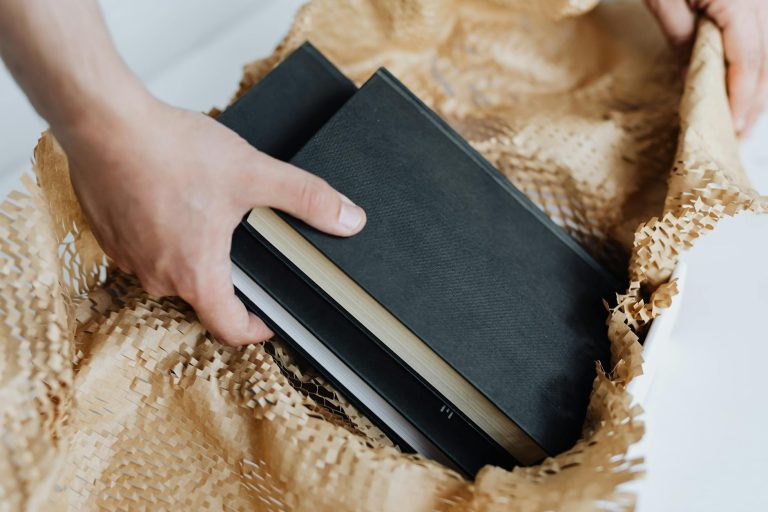 Close-up of hands packing hardcover books in a cardboard box with perforated paper.