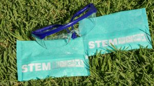 Blue protective goggles on grass with STEM packaging emphasizing education and safety.