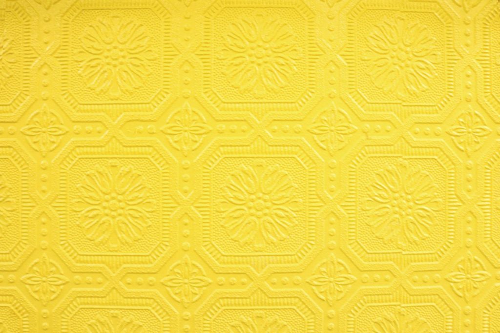 Close-up of a decorative yellow embossed wallpaper with an intricate repeating pattern.