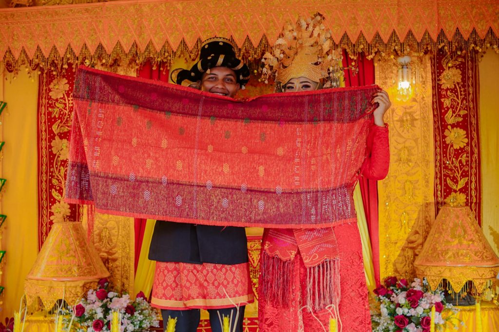 Indonesian couple in vibrant traditional wedding attire showcasing ornate textile.