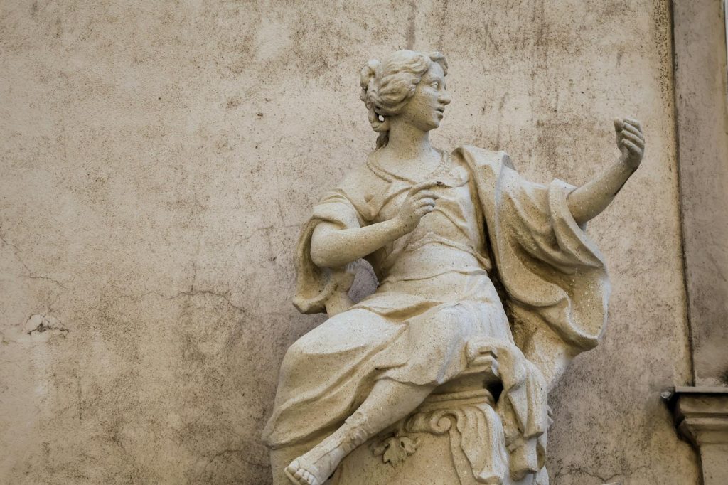 Detailed stone statue depicting a classic figure against a textured, weathered wall background.