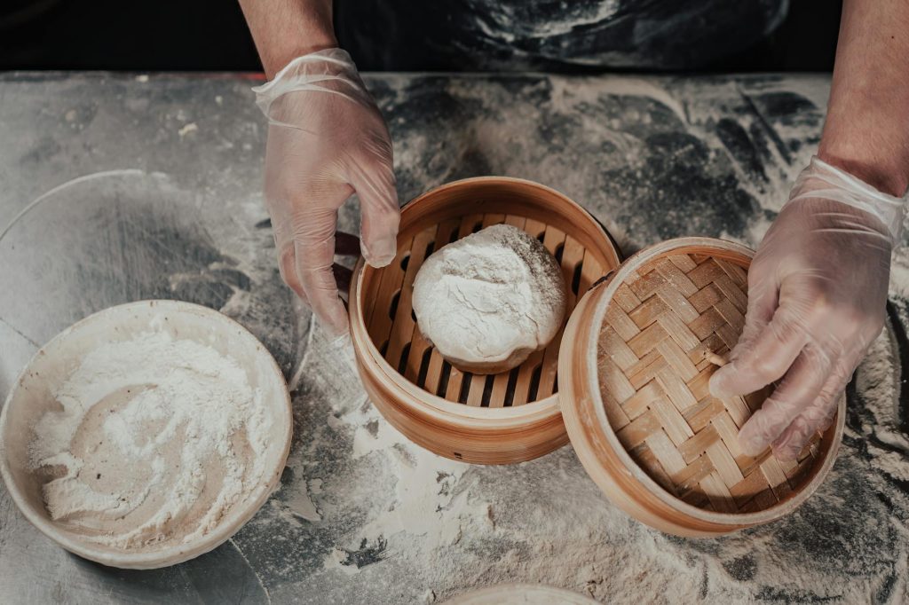 Hands preparing baozi dough in a bamboo steamer, showcasing traditional cooking.