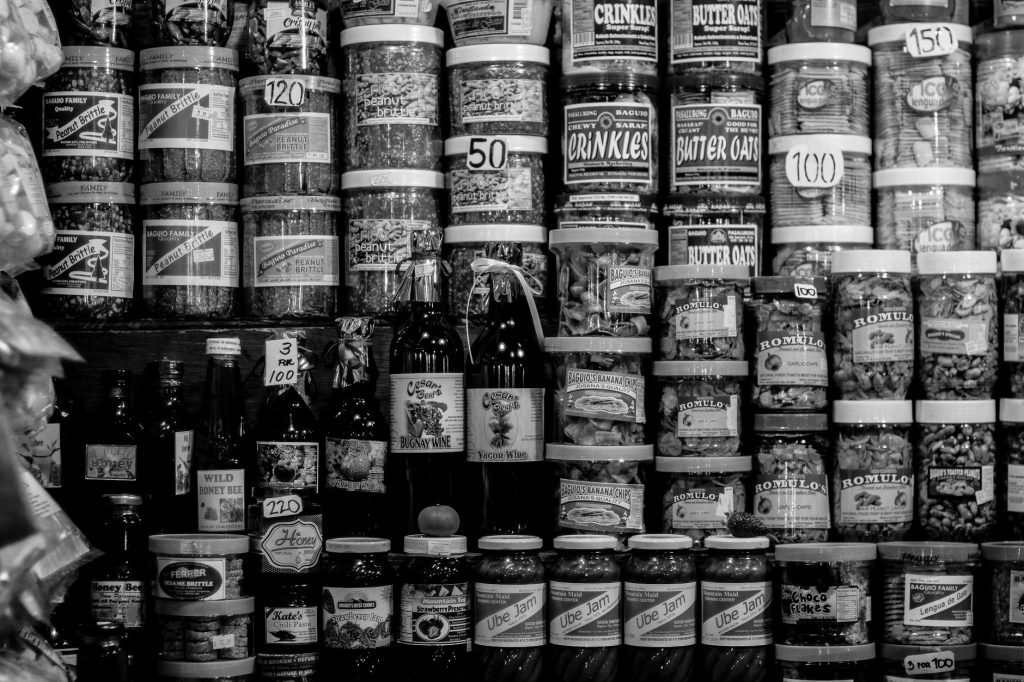 A black and white photo showcasing various food products stacked on market shelves, capturing local merchandise.