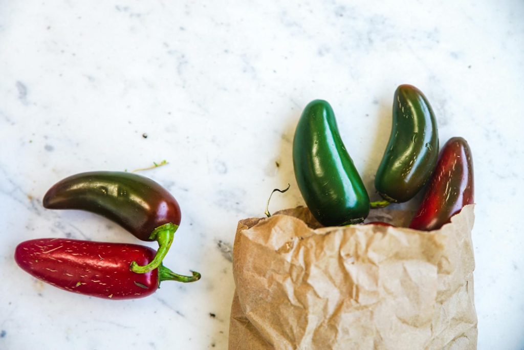 Close-up of vibrant jalapeƱo peppers spilling from a paper bag on a marble surface, perfect for spicy food concepts.