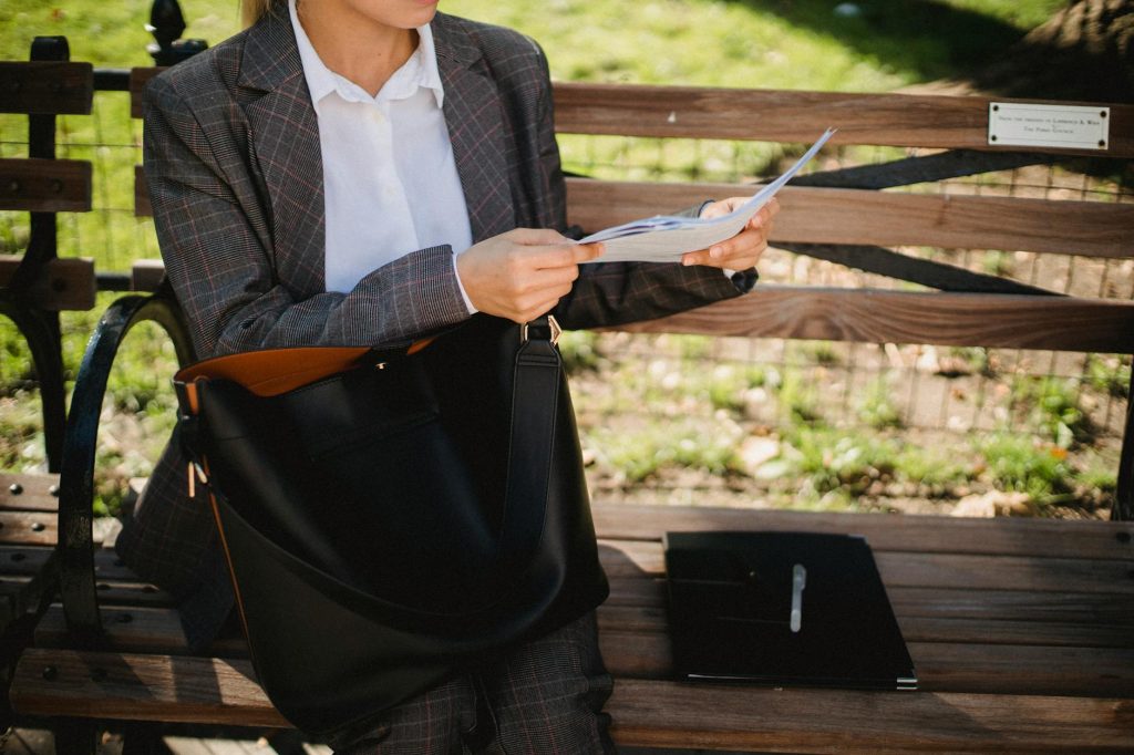 A woman in a suit reads documents on a park bench, showcasing professional fashion.