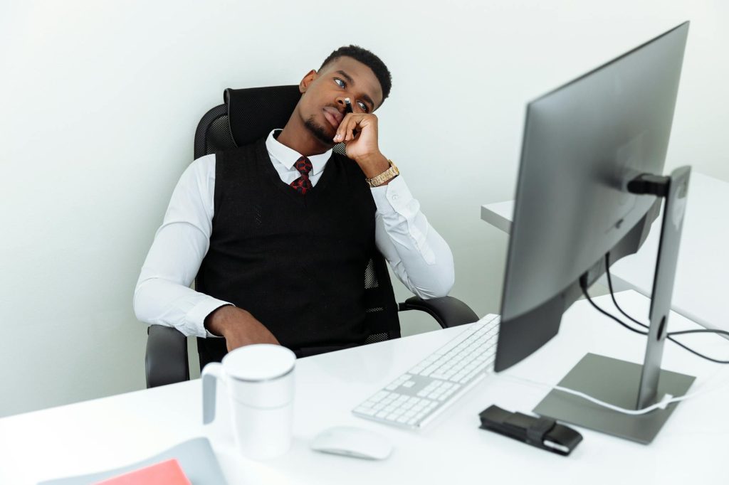 A man in business attire sits pensively at a desk with a computer, looking thoughtful.