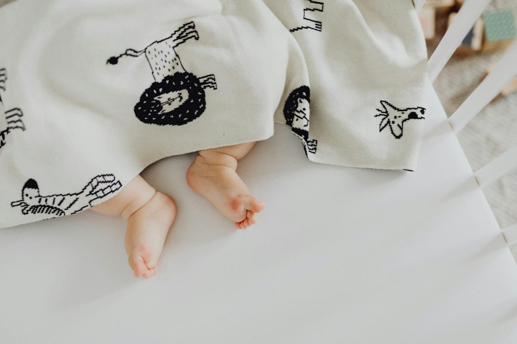 A close-up of a baby's feet poking out from under a blanket with animal prints, lying in a crib.