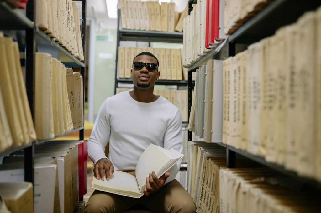 African American man with sunglasses reads a Braille book in a library.