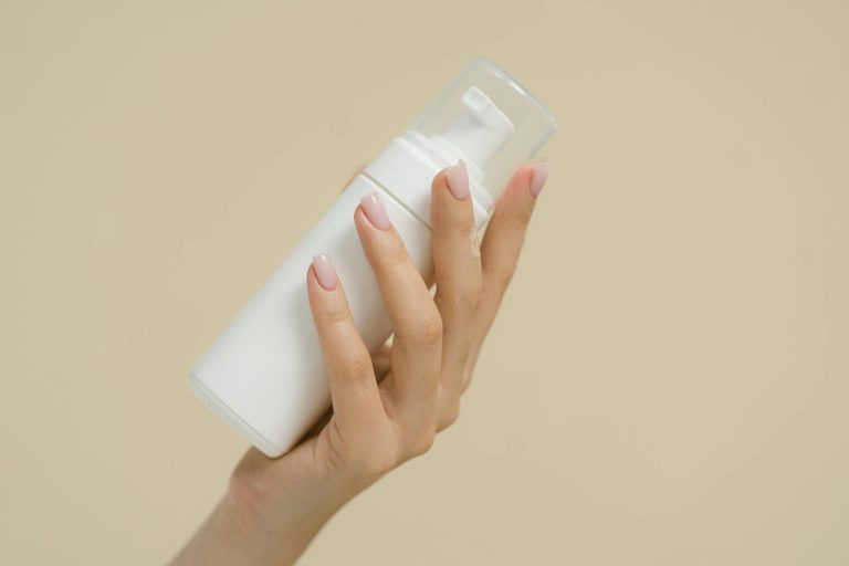 A close-up of a hand holding a white cosmetic bottle against a neutral background, perfect for product mockups and beauty industry use.
