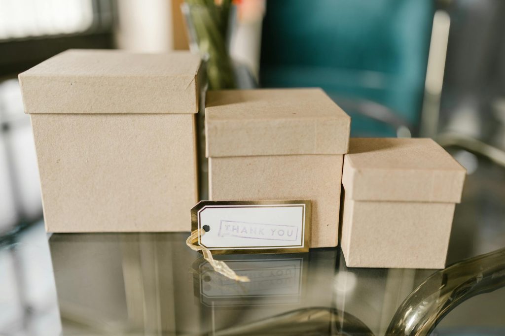 Three brown cardboard boxes on a glass table with a tag reading 'Thank You.', perfect for gifting concepts.