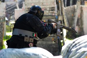 A player in full gear engages energetically in an outdoor paintball match.