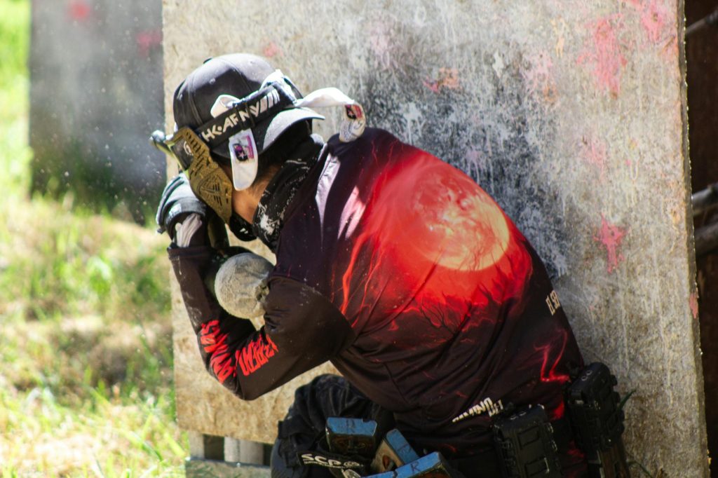 A paintball player in protective gear crouches behind cover, ready for action on the field.