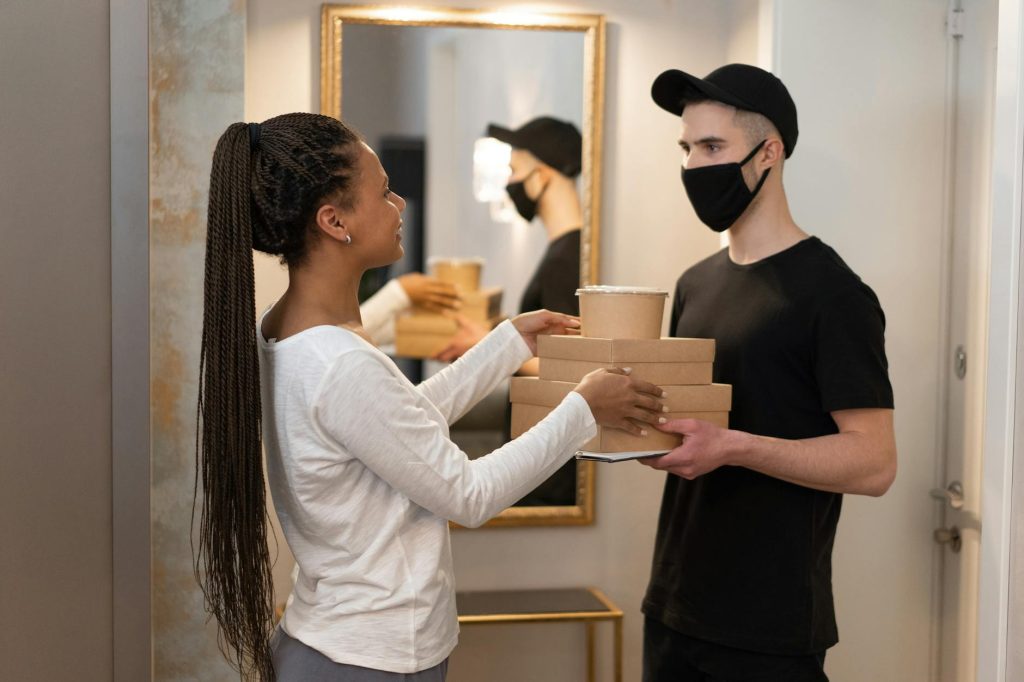 A woman receives a package from a masked delivery man in a modern home interior.
