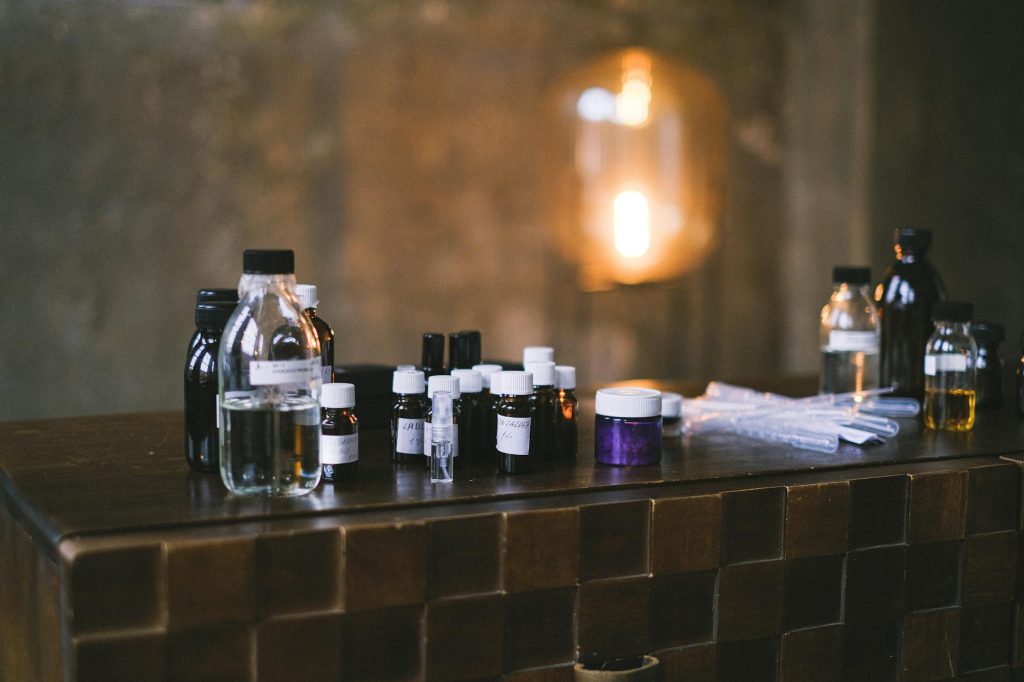 A variety of small glass bottles with a blurry background on a wooden counter in a dimly lit indoor setting.