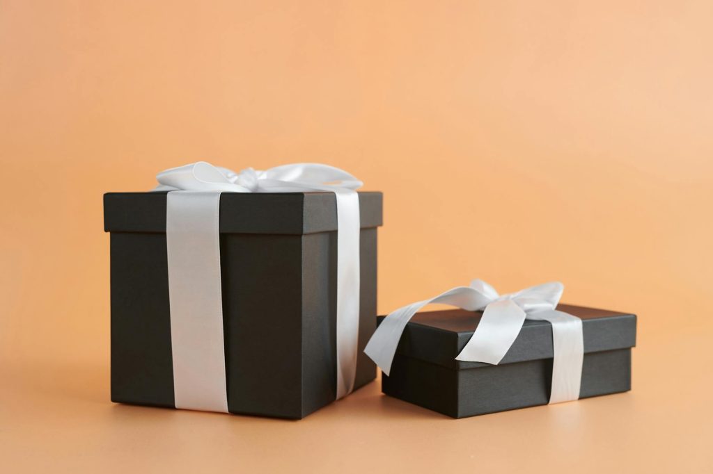 Two black gift boxes with white ribbons on a beige background, perfect for celebrations.
