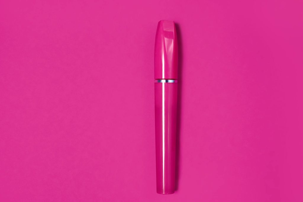 A striking pink mascara tube centered on a solid pink background, showcasing modern beauty packaging.