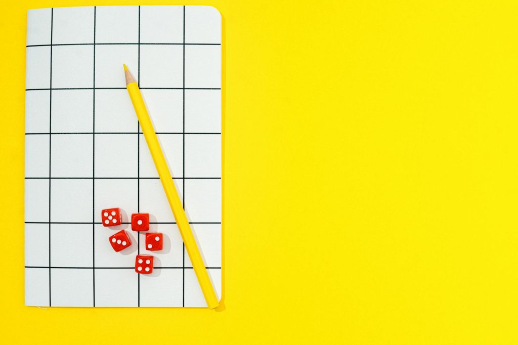 Grid notebook, pencil, and dice against a vibrant yellow backdrop with plenty of copy space.