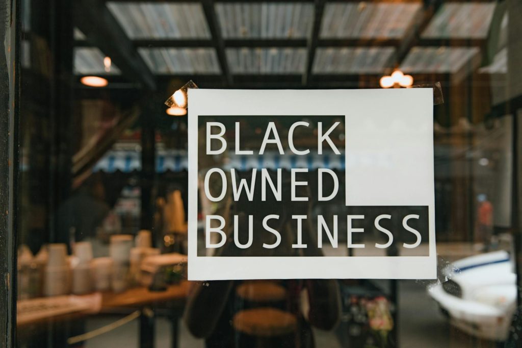 Black owned business sign taped on a window, seen from outside a store.