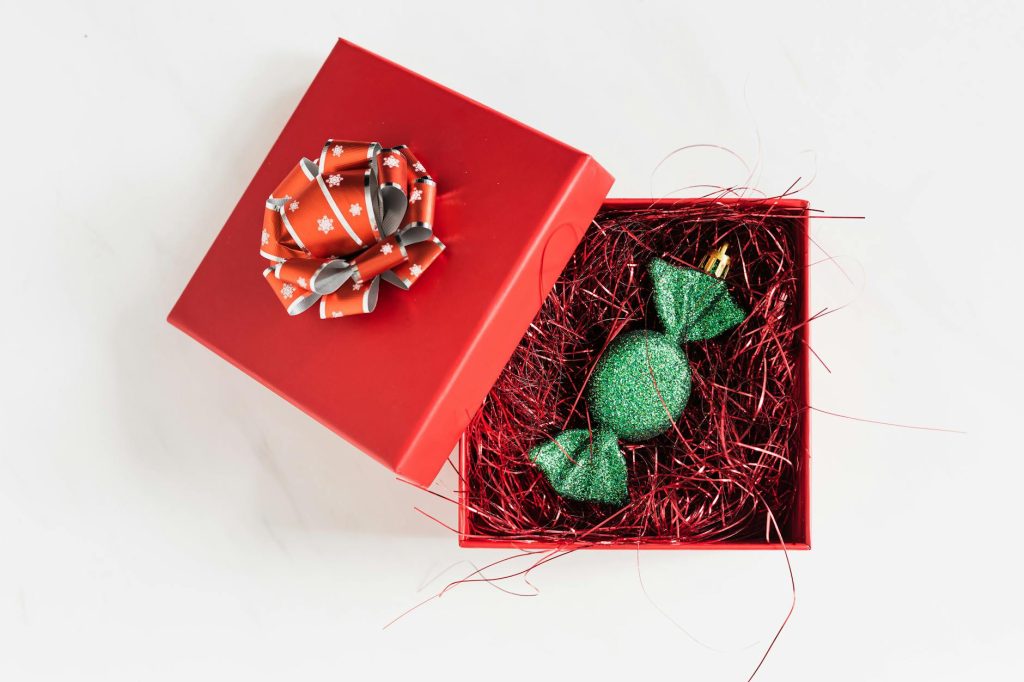 Open red gift box with a festive green glittery ornament inside on a white background, perfect for holiday themes.