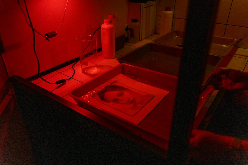A vintage photograph develops in a darkroom under red lighting, showcasing analog photography.