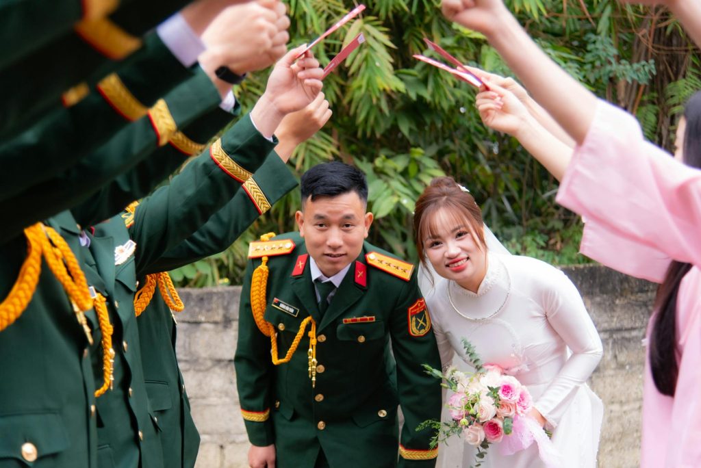A Vietnamese couple in traditional wedding and military attire surrounded by bridesmaids.