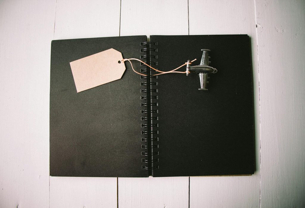 A black notebook with a miniature toy airplane and blank tag for customization or creativity.