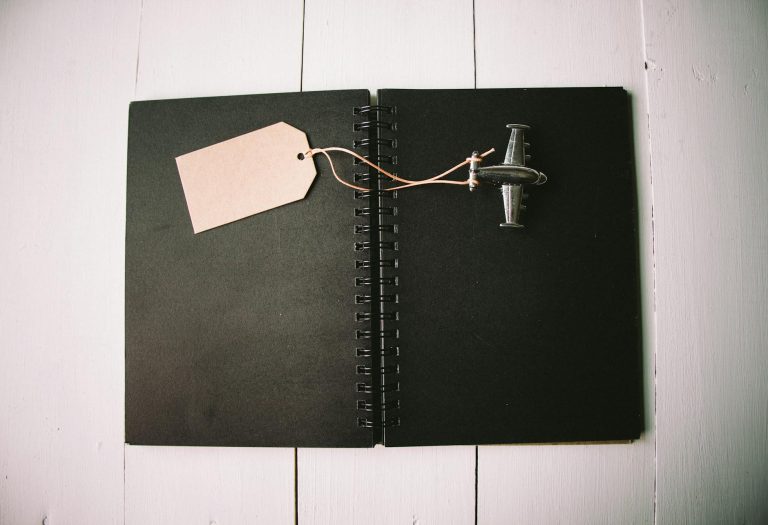A black notebook with a miniature toy airplane and blank tag for customization or creativity.