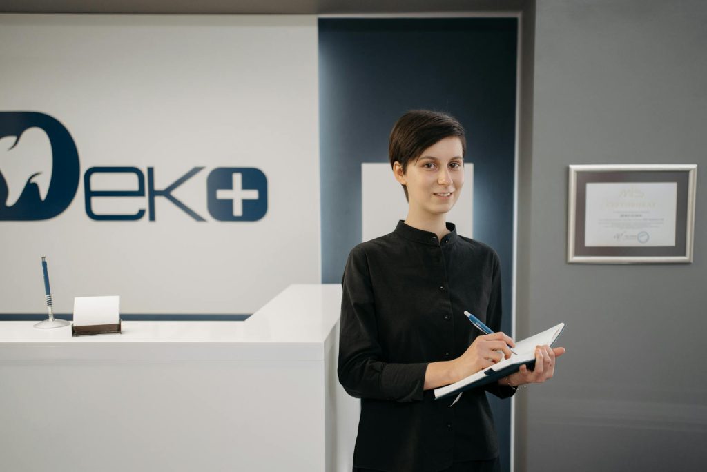 Smiling woman holding a notebook at a modern dentist office reception area.