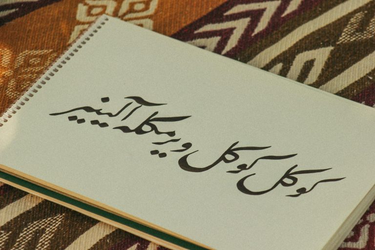 Notebook with Persian calligraphy on colorful patterned fabric background.