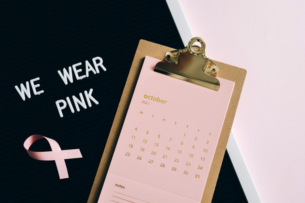 Flat lay image of calendar and pink ribbon for breast cancer awareness in October.