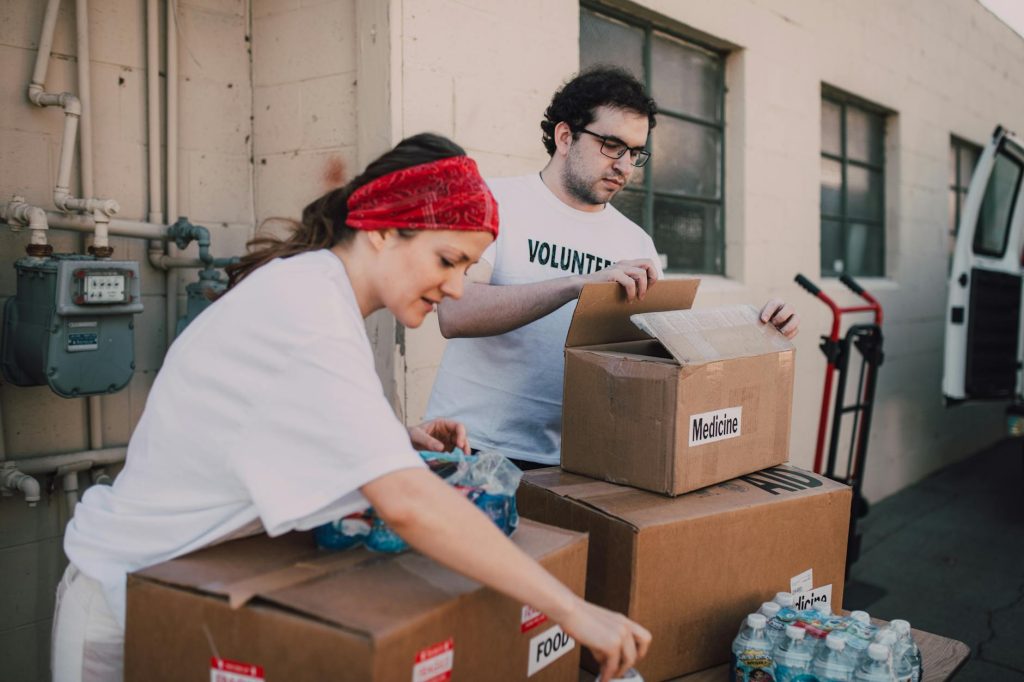 Two volunteers sorting medicine and food supplies outdoors, showcasing generosity and teamwork.