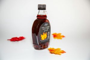 Close-up of a Canadian maple syrup bottle with colorful autumn leaves on white background.